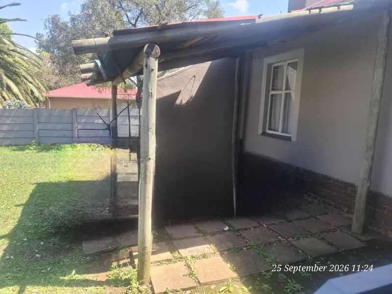 A covered outdoor patio area featuring a timber pole pergola structure, paved flooring, and direct access to the rear garden.