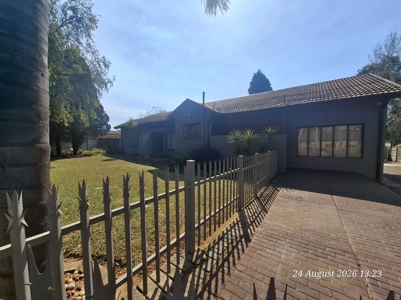 Front view of the house featuring a paved driveway, metal security fencing, and a well-maintained lawn area.