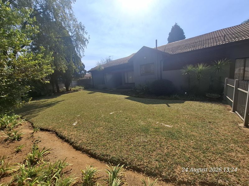 A view of the rear exterior of the house featuring a well-maintained lawn, garden landscaping, and perimeter fencing.