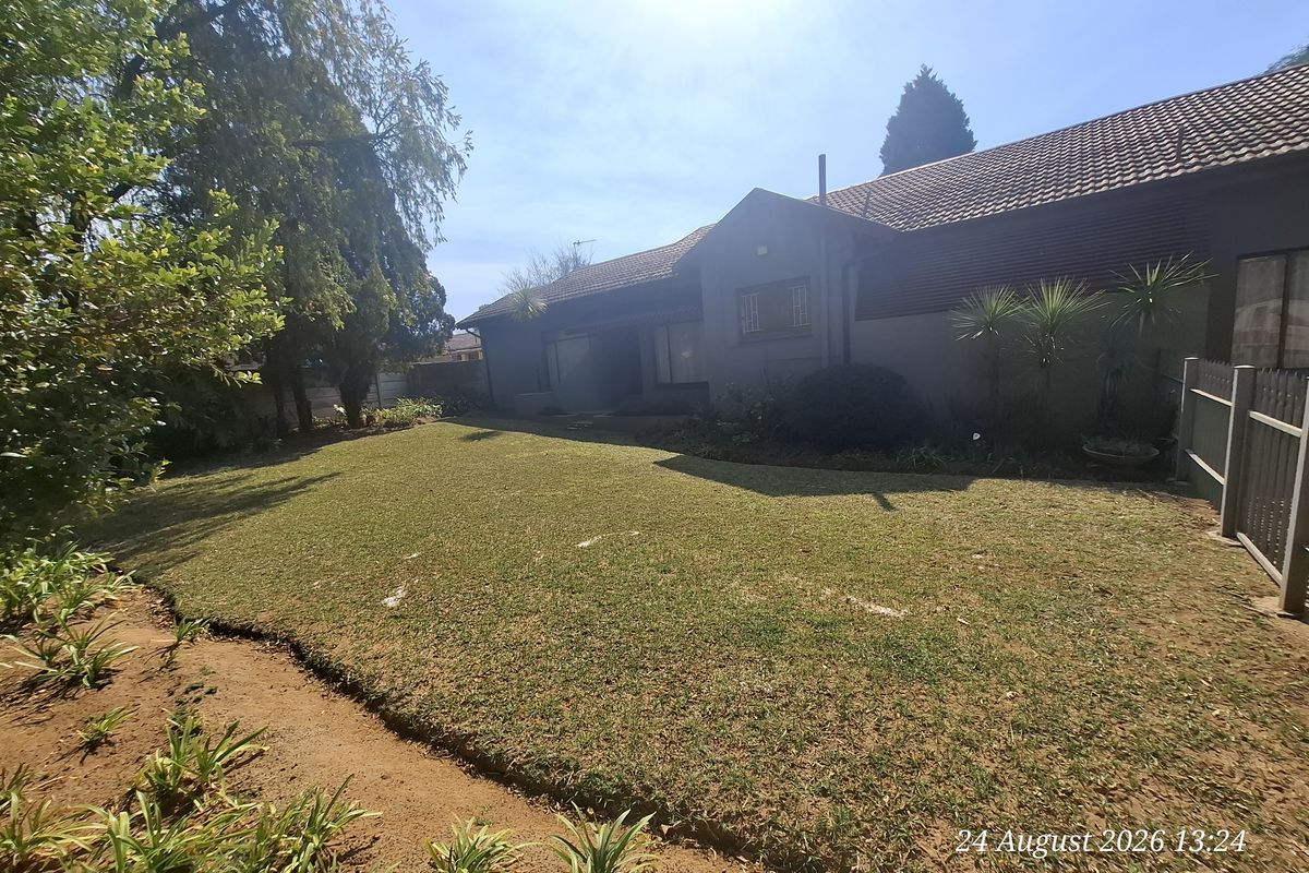 A view of the rear exterior of the house featuring a well-maintained lawn, garden landscaping, and perimeter fencing.