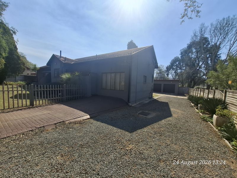 Front exterior view of the house featuring a paved and gravel driveway, perimeter fencing, and a detached double garage.