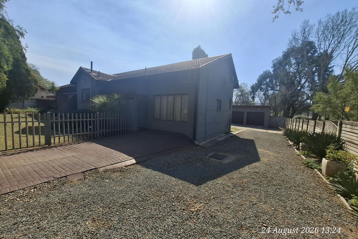 Front exterior view of the house featuring a paved and gravel driveway, perimeter fencing, and a detached double garage.