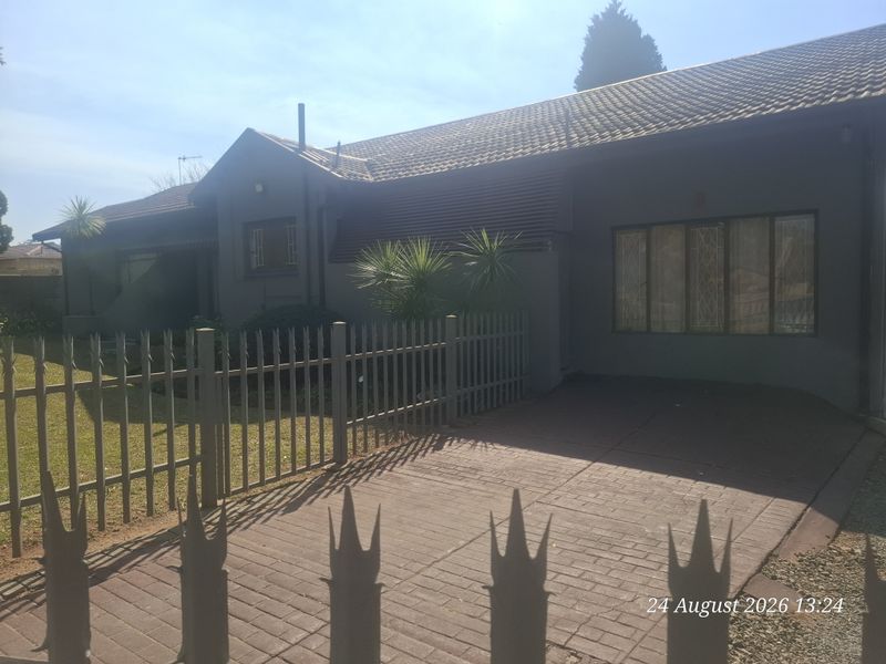 Front view of a residential property featuring a paved driveway, metal security fencing, and a tiled roof facade.