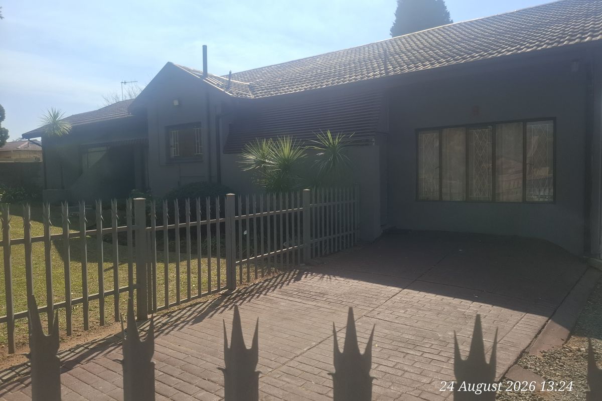 Front view of a residential property featuring a paved driveway, metal security fencing, and a tiled roof facade.