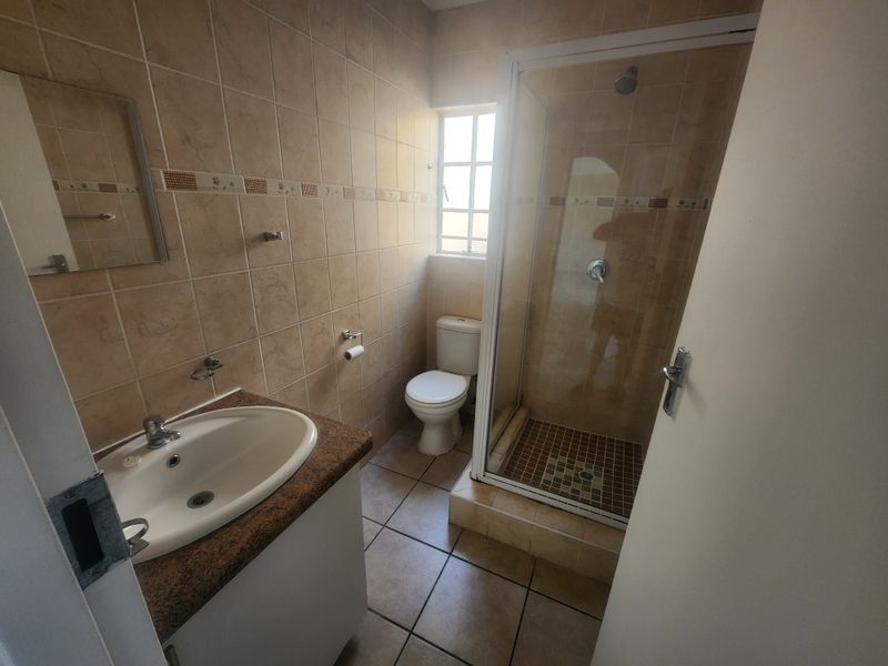 A functional bathroom featuring a shower enclosure, vanity basin, and toilet with neutral wall and floor tiling.
