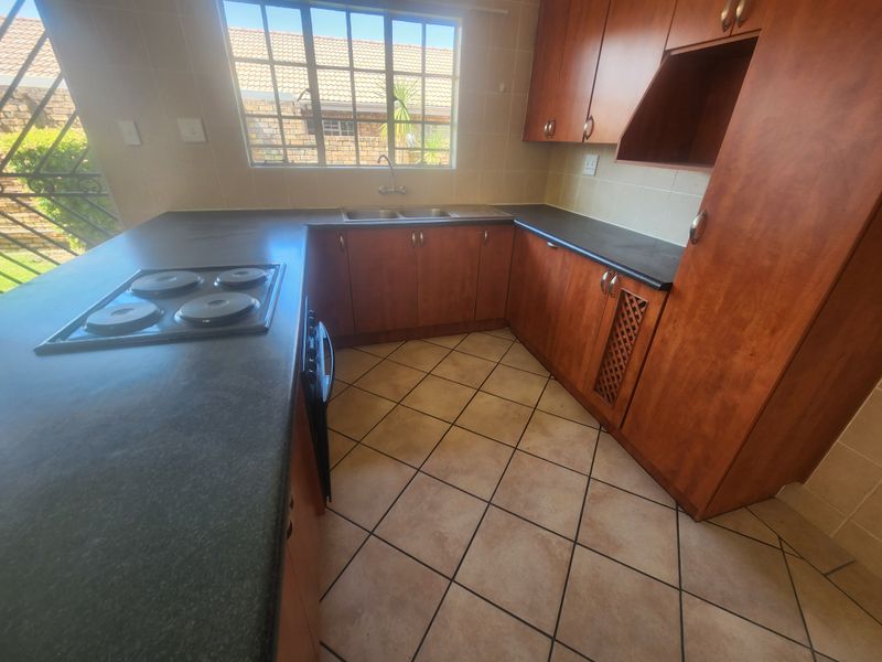 A functional kitchen featuring wooden cabinetry, dark laminate countertops, an integrated electric hob, and tiled flooring with a window overlooking the exterior.