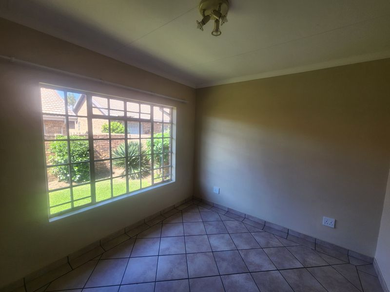 A bright, empty bedroom featuring tiled flooring, neutral walls, and a large window providing natural light and a view of the garden.