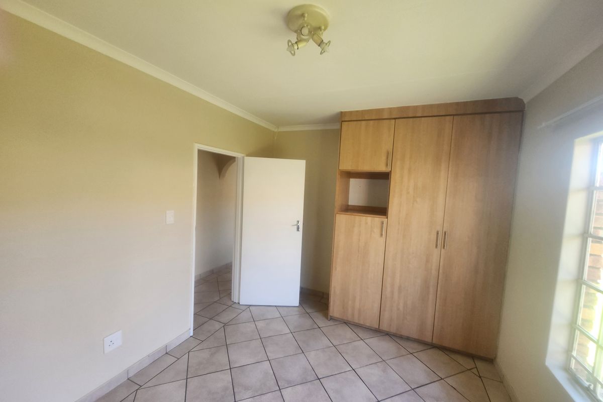 A clean, empty bedroom featuring tiled flooring, a built-in wooden wardrobe, and a window with security bars.
