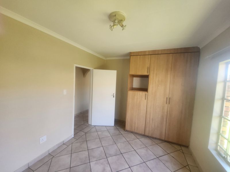 A clean, empty bedroom featuring tiled flooring, a built-in wooden wardrobe, and a window with security bars.