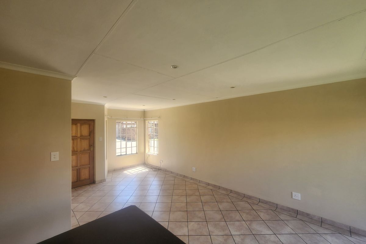 A spacious, empty living area featuring neutral wall tones, tiled flooring, and recessed lighting, providing a versatile blank canvas for interior design.