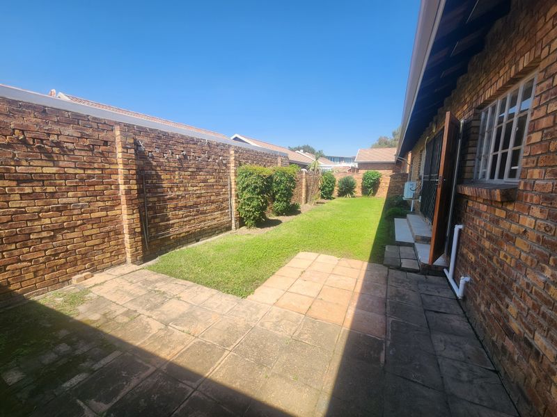 A private rear garden featuring a paved patio area, a well-maintained lawn, and high brick boundary walls for added privacy.