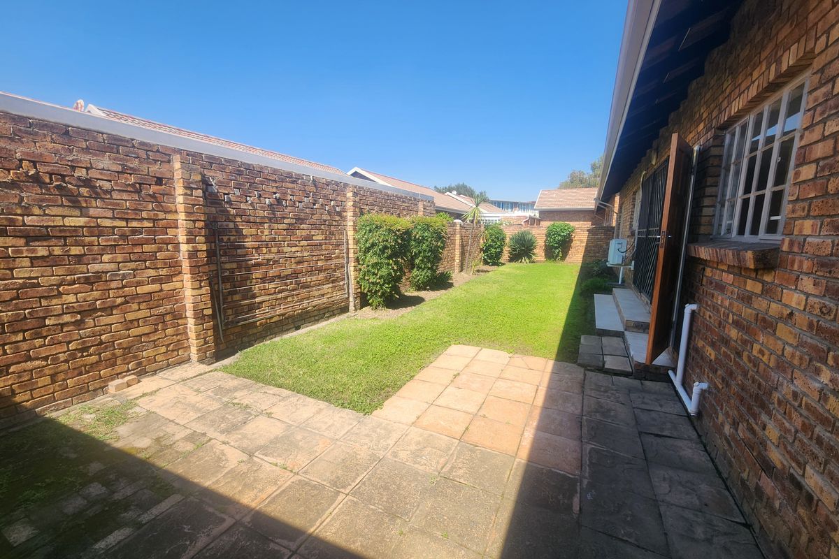 A private rear garden featuring a paved patio area, a well-maintained lawn, and high brick boundary walls for added privacy.
