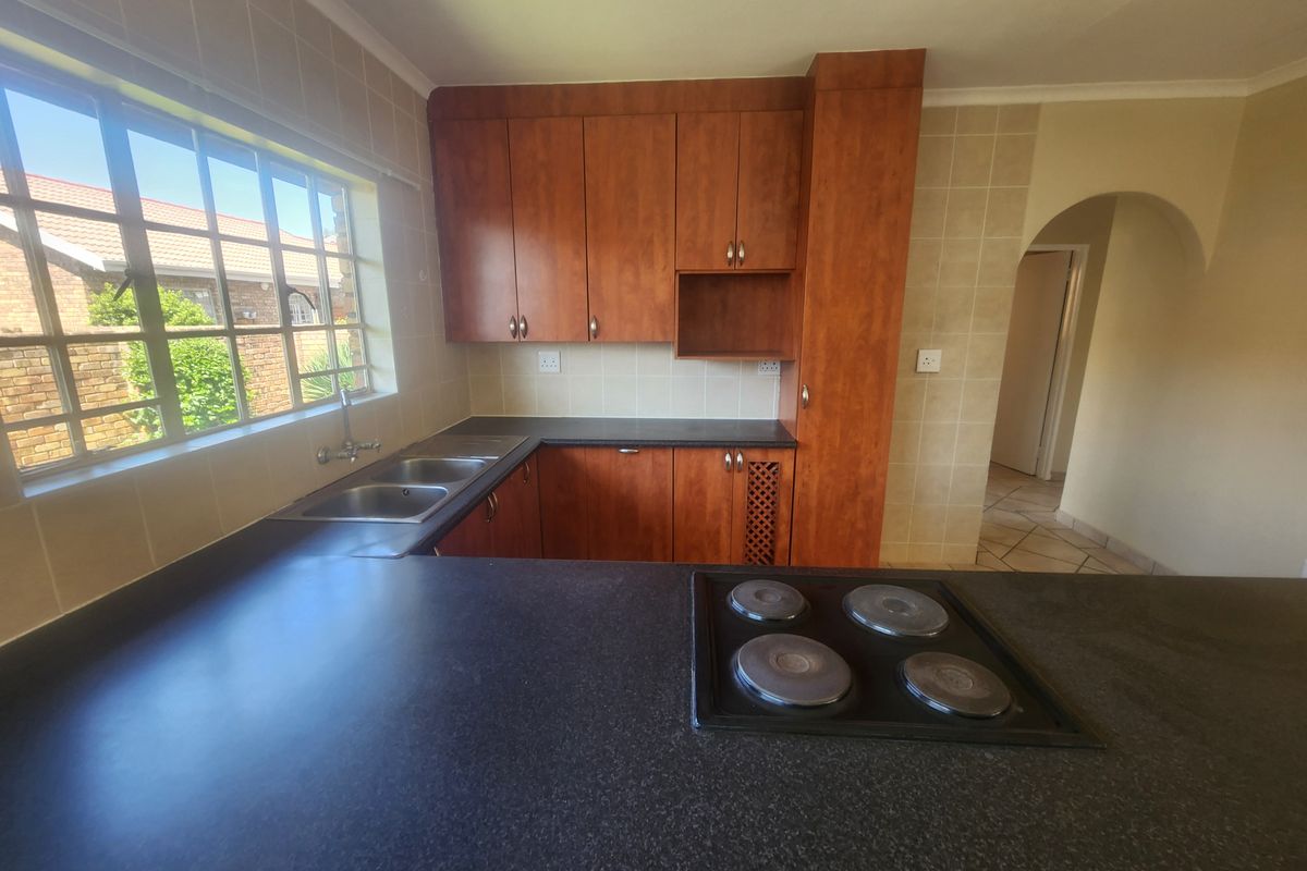A functional kitchen featuring wooden cabinetry, dark laminate countertops, a built-in electric hob, and a double sink with a window view.