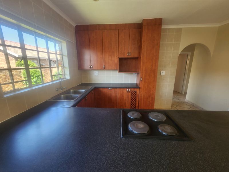 A functional kitchen featuring wooden cabinetry, dark laminate countertops, a built-in electric hob, and a double sink with a window view.