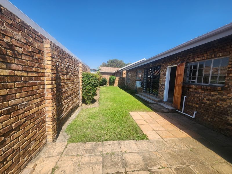A private rear garden featuring a paved patio area, established lawn, and face brick exterior walls with secure access points.