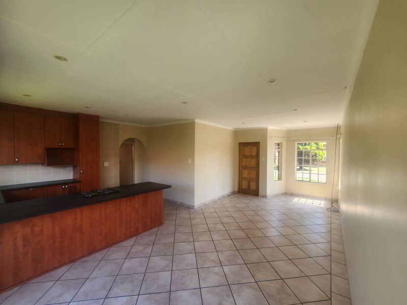 Spacious open-plan living and kitchen area featuring tiled flooring, built-in cabinetry with a hob, and natural light through large windows.