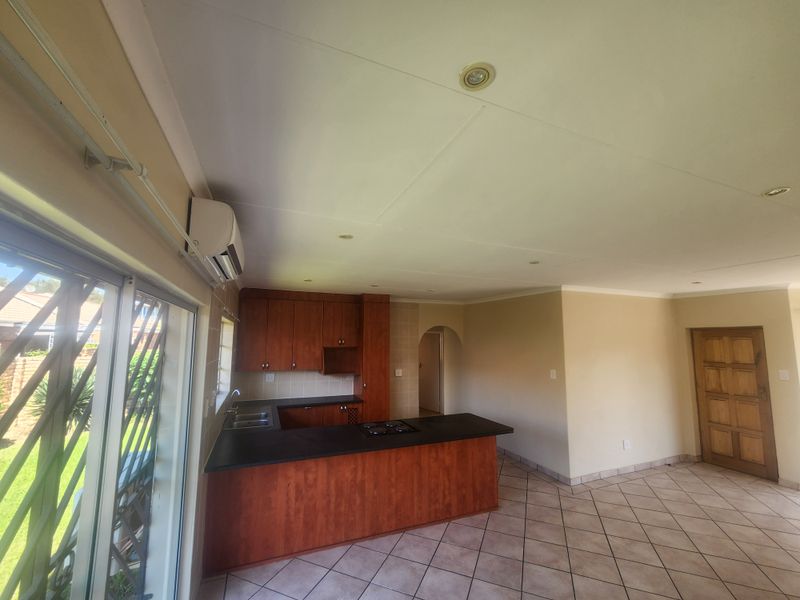 Open-plan kitchen and living area featuring wooden cabinetry, dark countertops, tiled flooring, and direct access to the outdoor space via sliding doors.