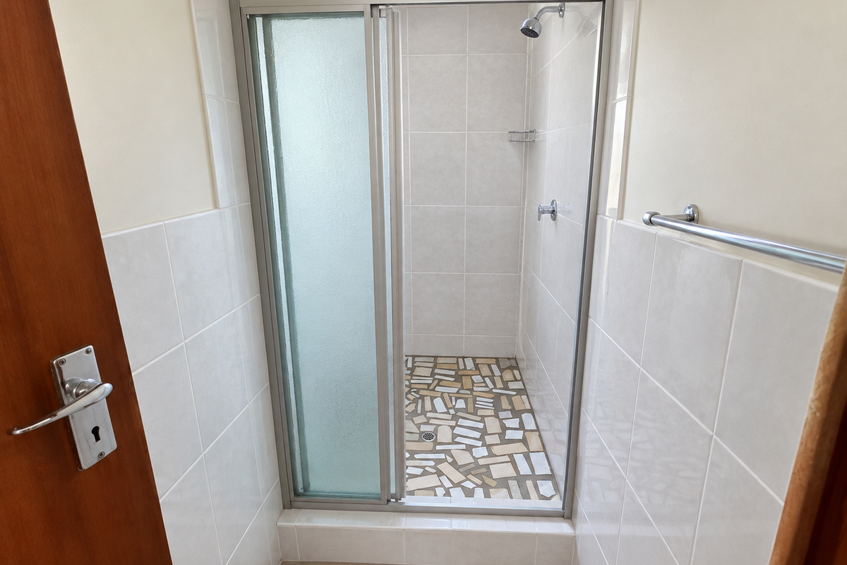 A clean bathroom shower area featuring a glass enclosure, tiled walls, and a decorative tiled shower floor.