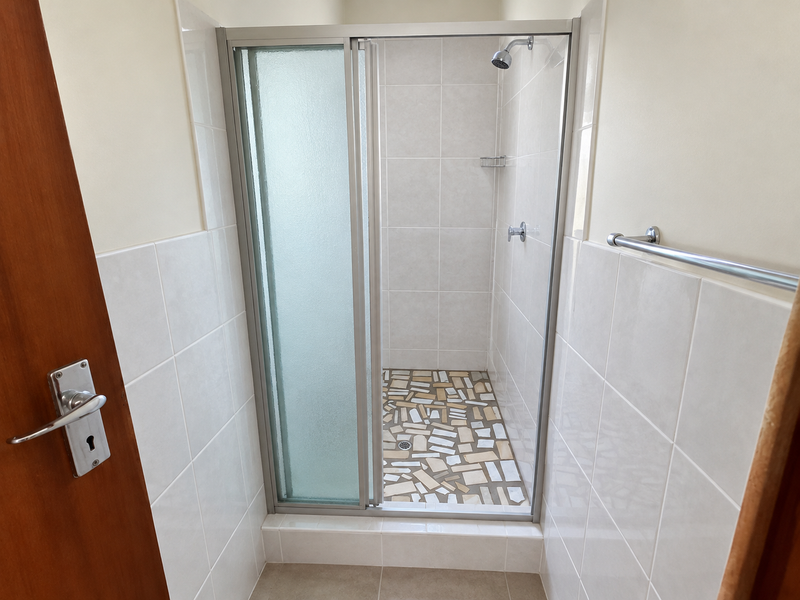A clean bathroom shower area featuring a glass enclosure, tiled walls, and a decorative tiled shower floor.