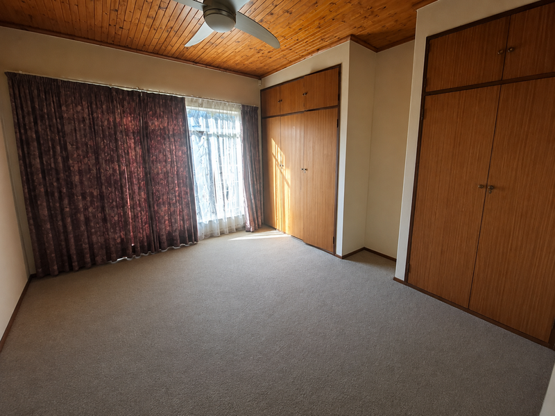 Spacious bedroom featuring built-in wooden cupboards, a timber-clad ceiling with a ceiling fan, and neutral carpeting.