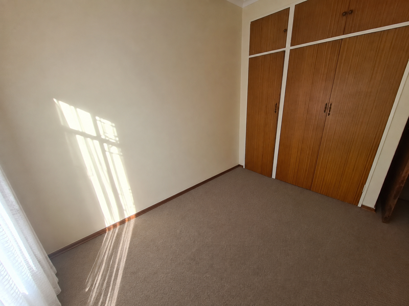 An empty bedroom featuring neutral walls, carpeted flooring, and built-in wooden cupboards.