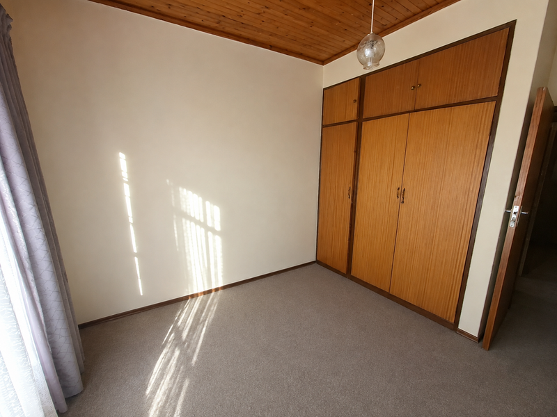 A bright, empty bedroom featuring built-in wooden cupboards, a classic timber tongue and groove ceiling, and neutral carpeting.
