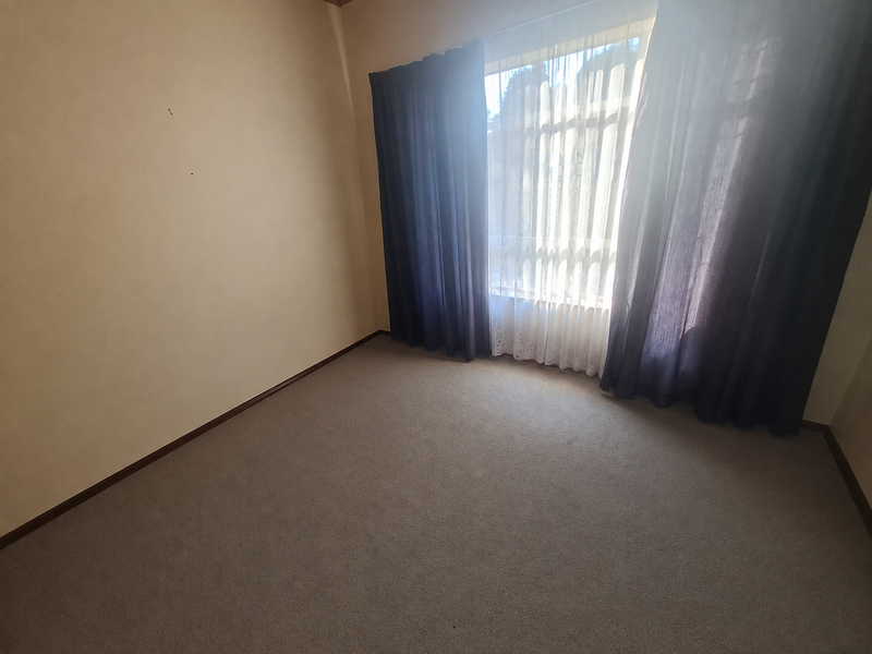 An empty bedroom featuring neutral carpet flooring and large windows with installed curtain tracks, offering a blank canvas for personalization.