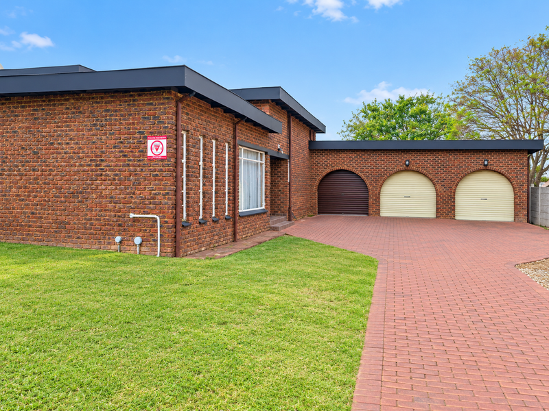 A well-maintained face brick house featuring a triple garage with roller shutter doors and a spacious paved driveway set on a neat lawn.