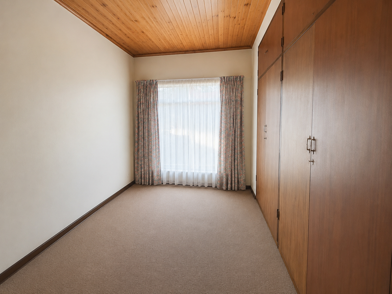 A clean, empty bedroom featuring built-in wooden cupboards, a warm timber-paneled ceiling, and neutral carpeting, offering a versatile space ready for personalization.