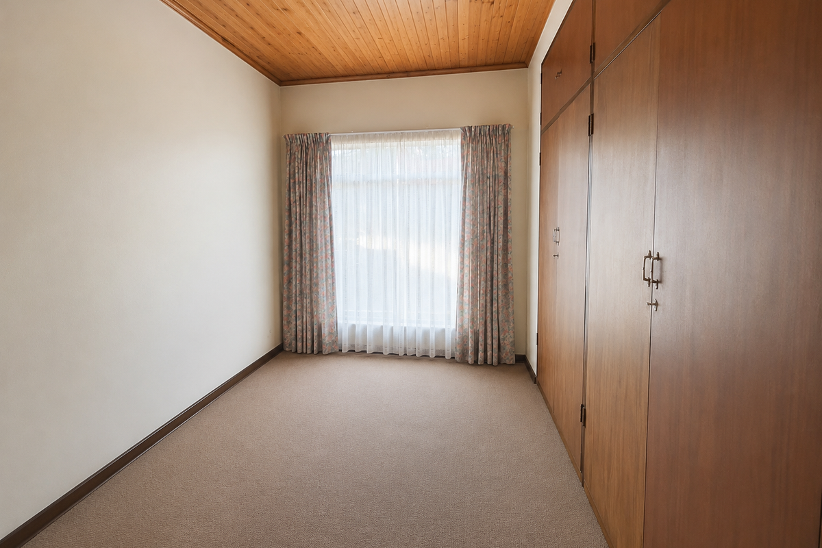 A clean, empty bedroom featuring built-in wooden cupboards, a warm timber-paneled ceiling, and neutral carpeting, offering a versatile space ready for personalization.
