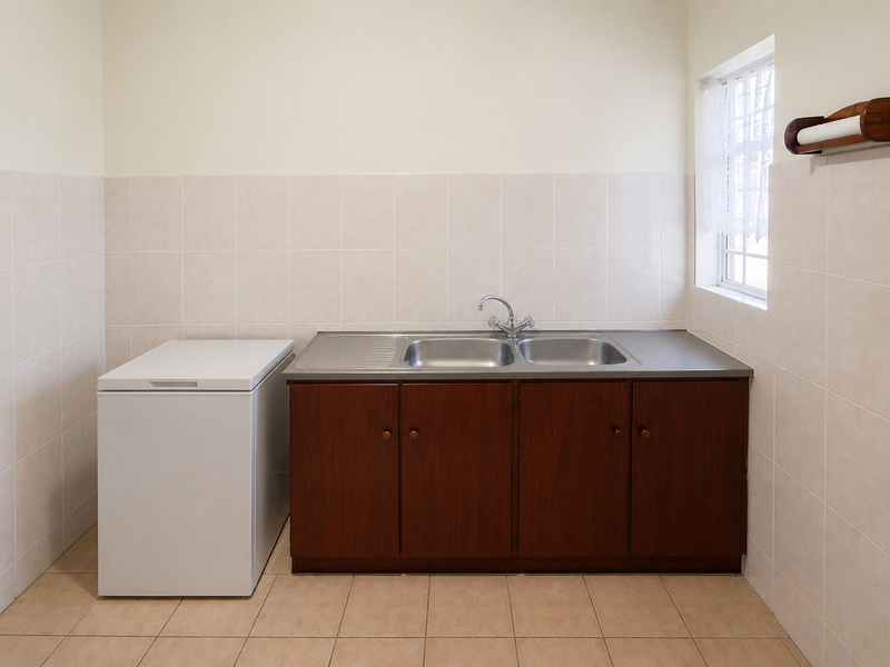 A functional laundry room featuring a stainless steel double sink, built-in wooden cabinetry, and neutral tiled walls and flooring.