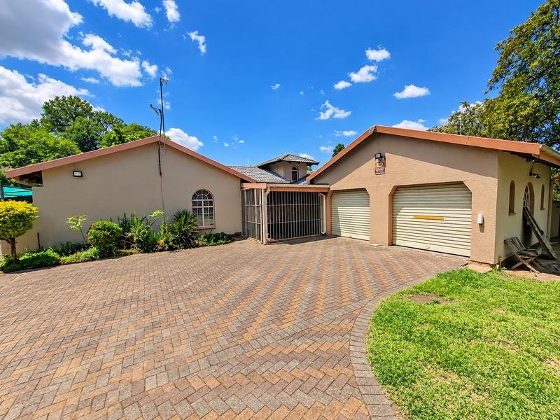Front exterior view of the property featuring a paved driveway, double garage with roll-up doors, and established garden surroundings.