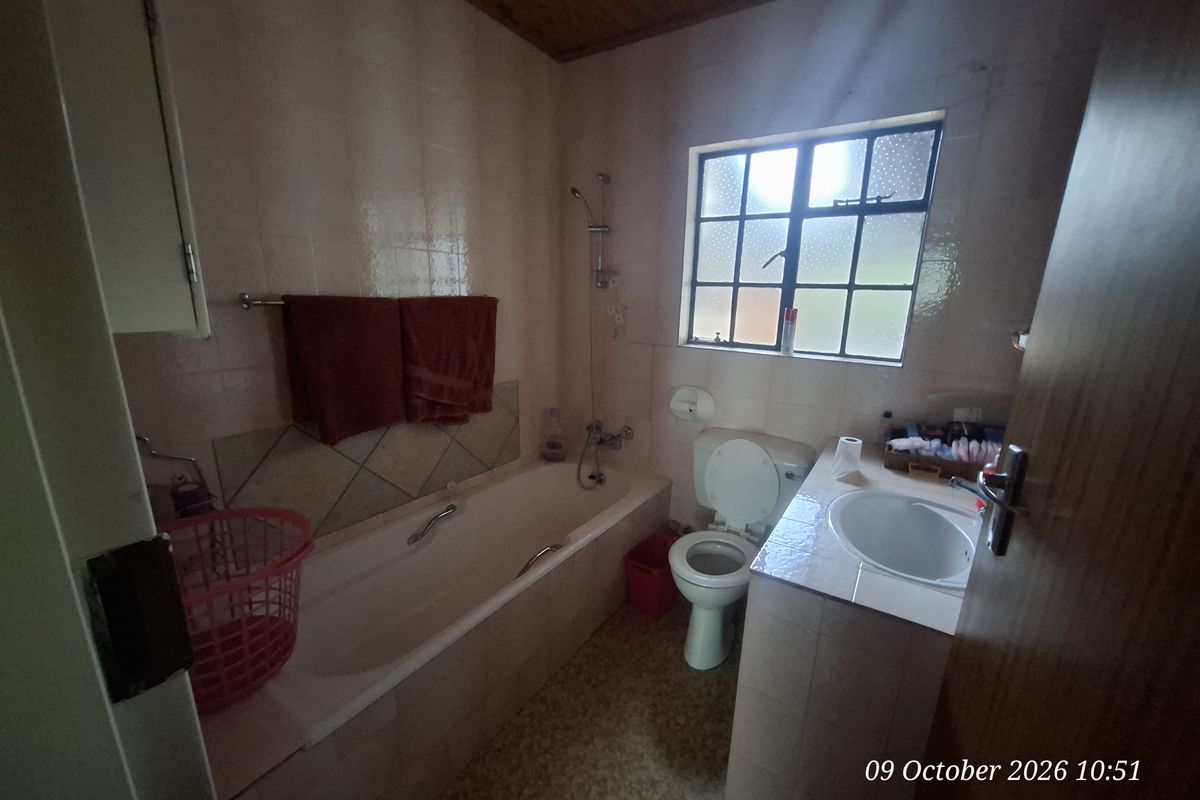 A dated bathroom featuring a bathtub, toilet, and vanity basin with tiled walls and a timber ceiling.