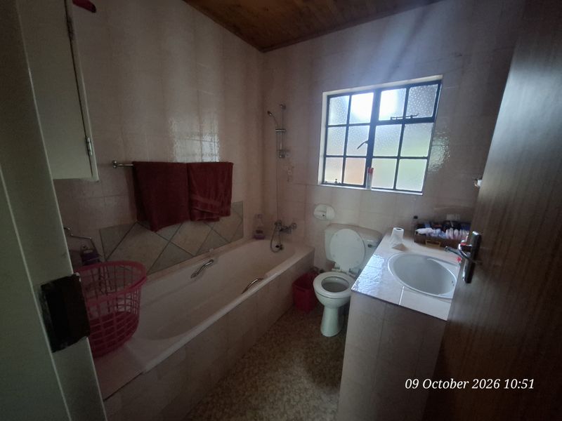 A dated bathroom featuring a bathtub, toilet, and vanity basin with tiled walls and a timber ceiling.