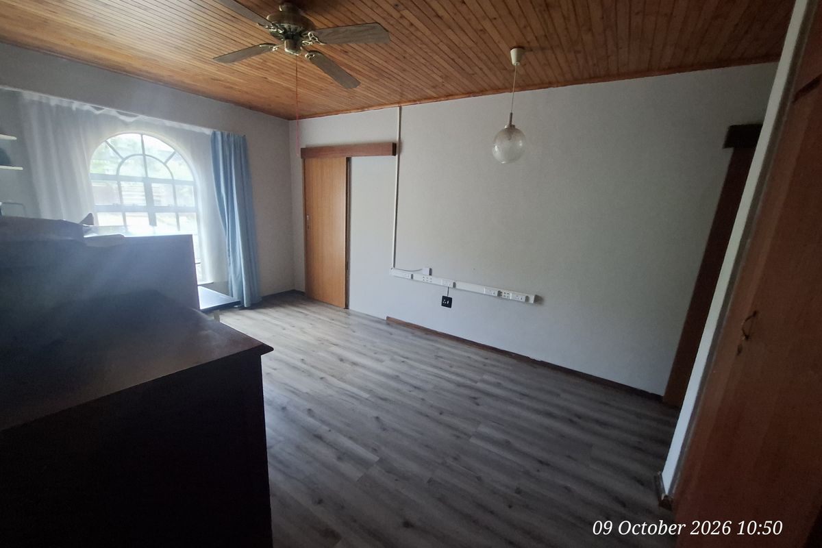 A vacant bedroom featuring timber ceiling paneling, laminate flooring, and an arched window, with surface-mounted electrical trunking along the wall.