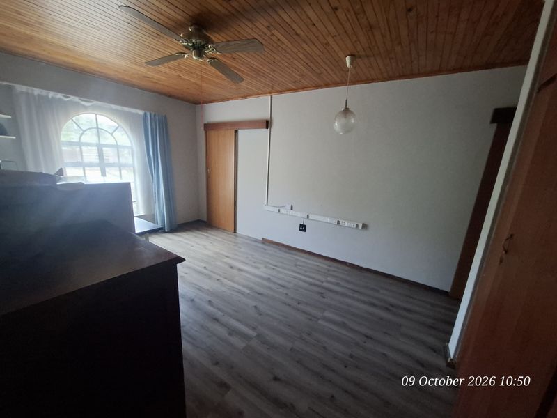 A vacant bedroom featuring timber ceiling paneling, laminate flooring, and an arched window, with surface-mounted electrical trunking along the wall.