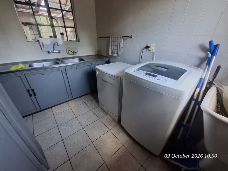 Functional laundry room featuring a double stainless steel sink, built-in cabinetry, and tiled surfaces, providing a practical space for household utility tasks.
