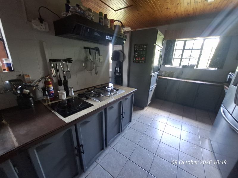A functional kitchen featuring dual cooktops, extractor fan, built-in cabinetry, and tiled flooring under a timber-paneled ceiling.