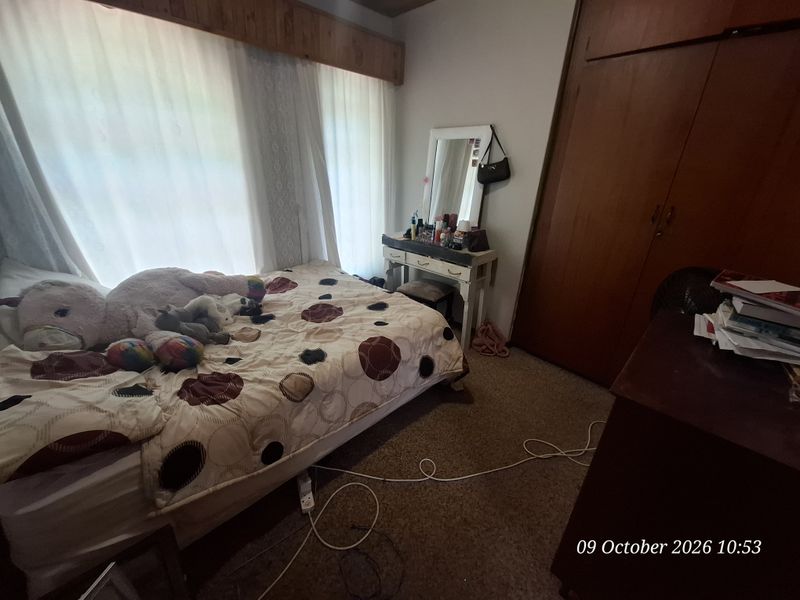 A bedroom featuring built-in wooden wardrobes, carpeted flooring, and a window with a wooden pelmet.