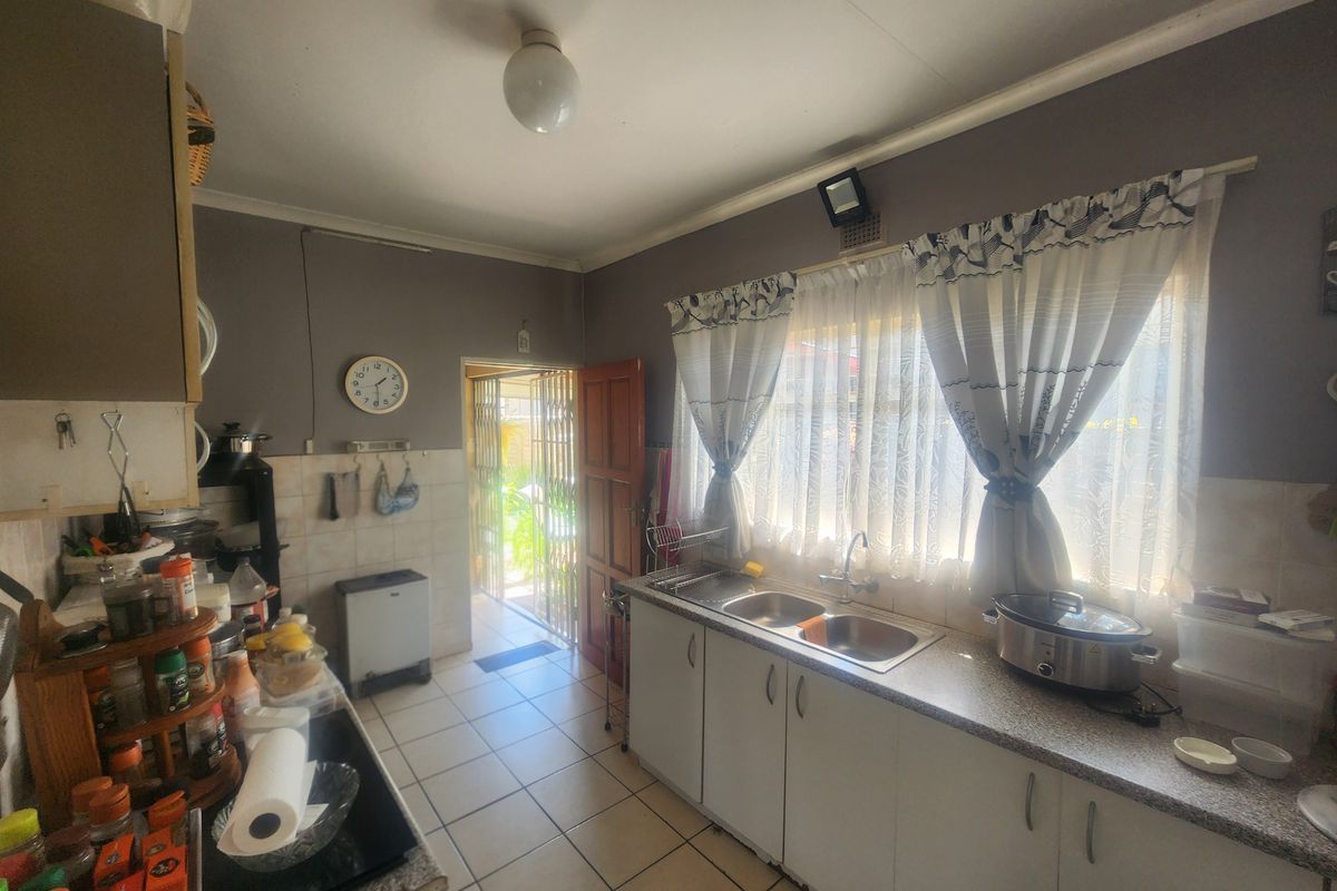 A functional kitchen featuring double bowl stainless steel sink, laminate countertops, and tiled flooring, with direct access to an exterior door.