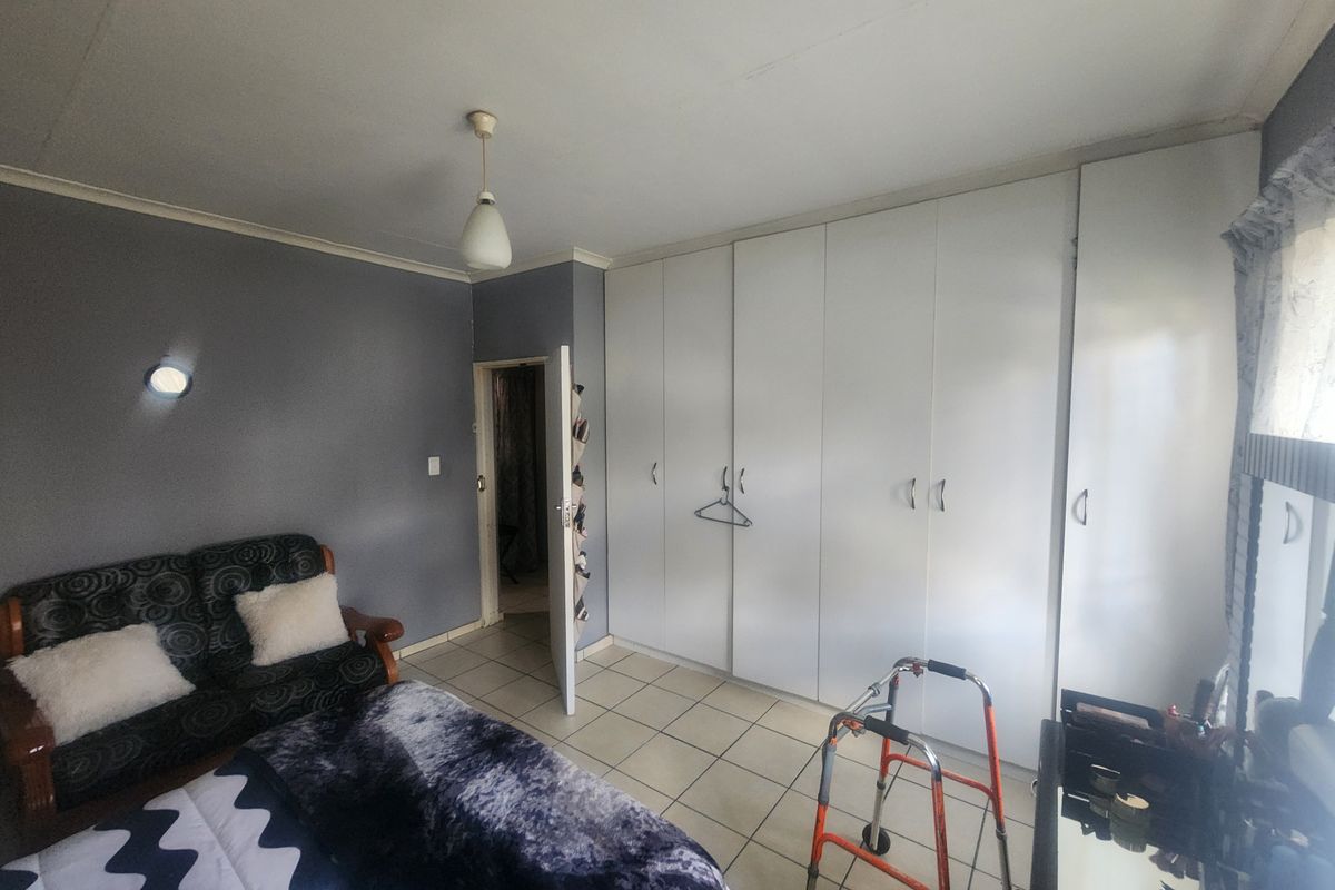 A bedroom featuring built-in cupboards, tiled flooring, and neutral wall finishes, providing a functional space with potential for cosmetic updates.