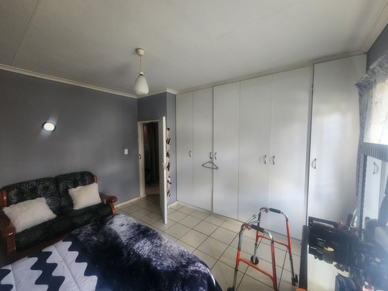 A bedroom featuring built-in cupboards, tiled flooring, and neutral wall finishes, providing a functional space with potential for cosmetic updates.