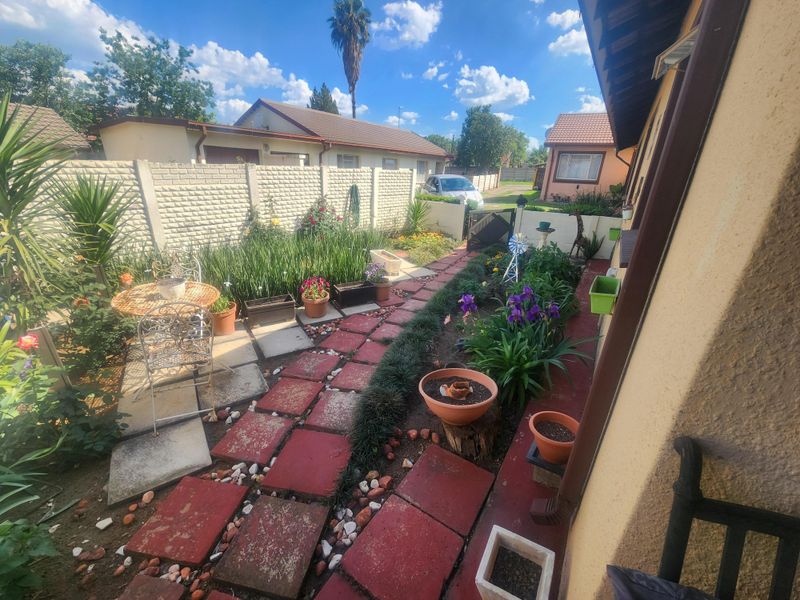 A private rear garden area featuring a paved walkway, established garden beds, and a secure precast concrete boundary wall.