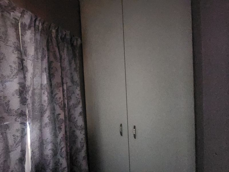A bedroom interior featuring a built-in wardrobe and window with curtains.
