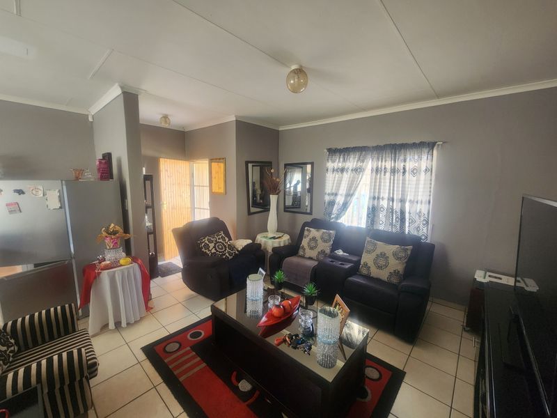 A comfortable living room featuring tiled flooring, neutral wall tones, and natural light, providing a functional and inviting space for relaxation.