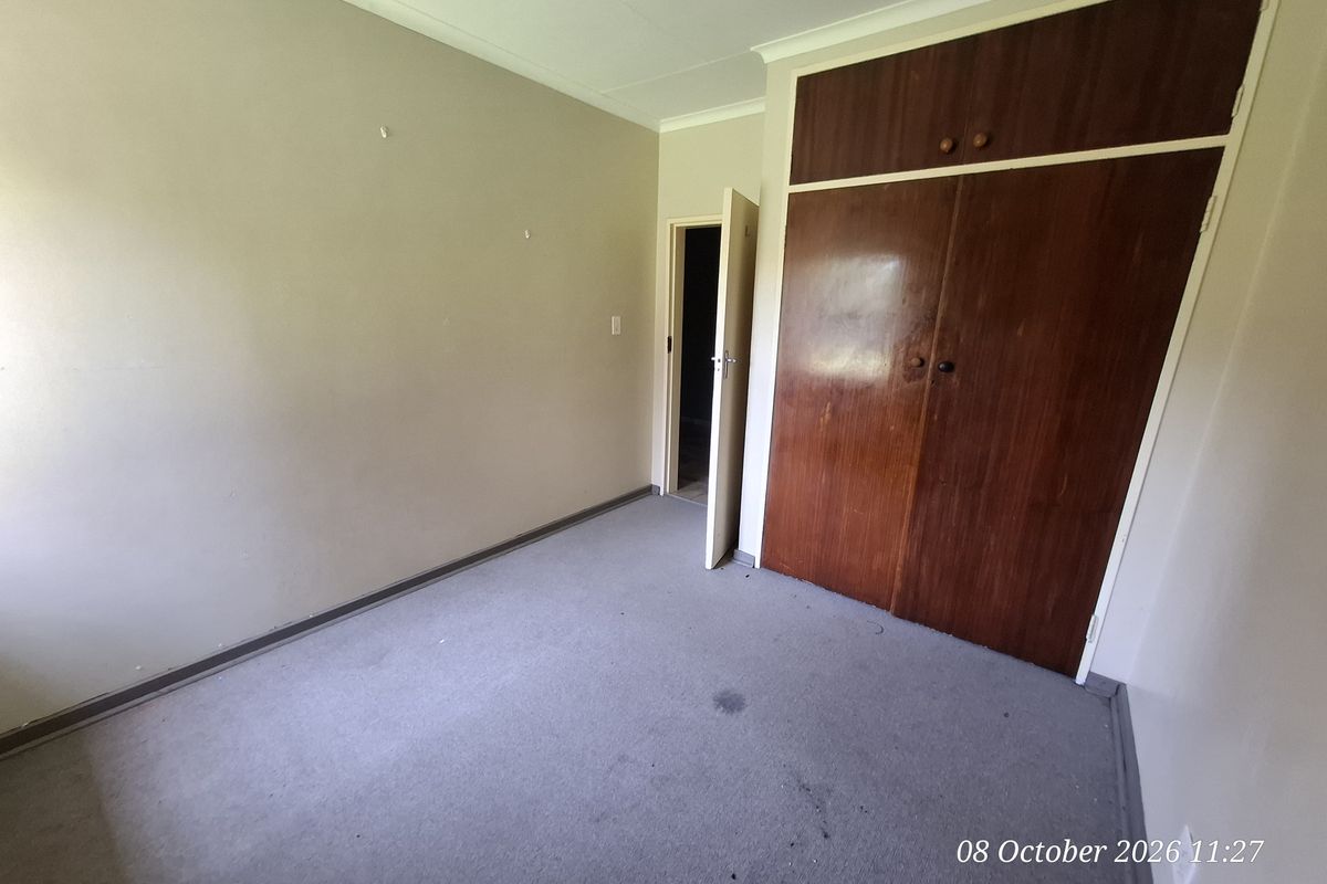 An empty bedroom featuring built-in wooden cupboards, carpeted flooring, and coved ceilings, offering a blank canvas for renovation or restyling.
