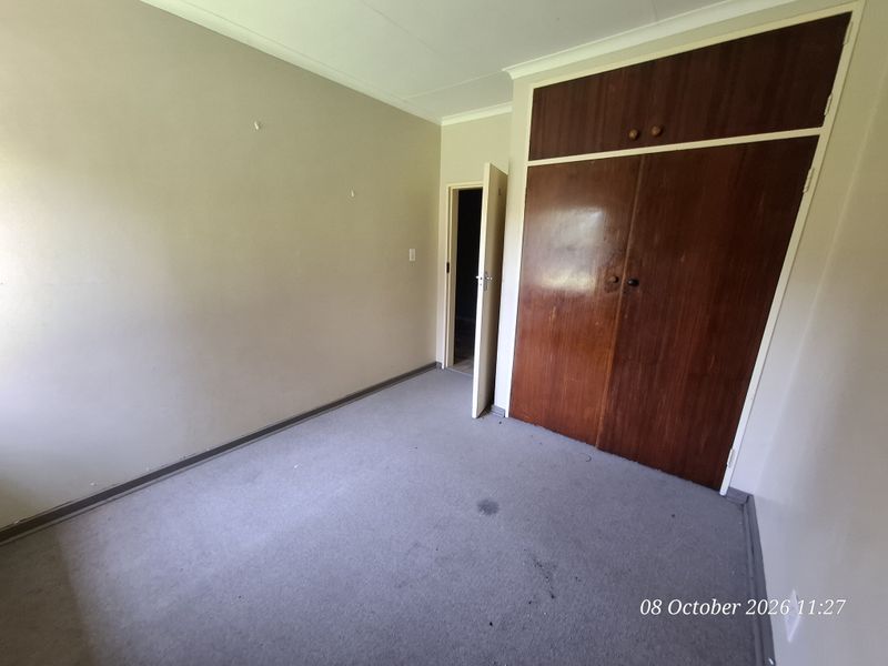 An empty bedroom featuring built-in wooden cupboards, carpeted flooring, and coved ceilings, offering a blank canvas for renovation or restyling.