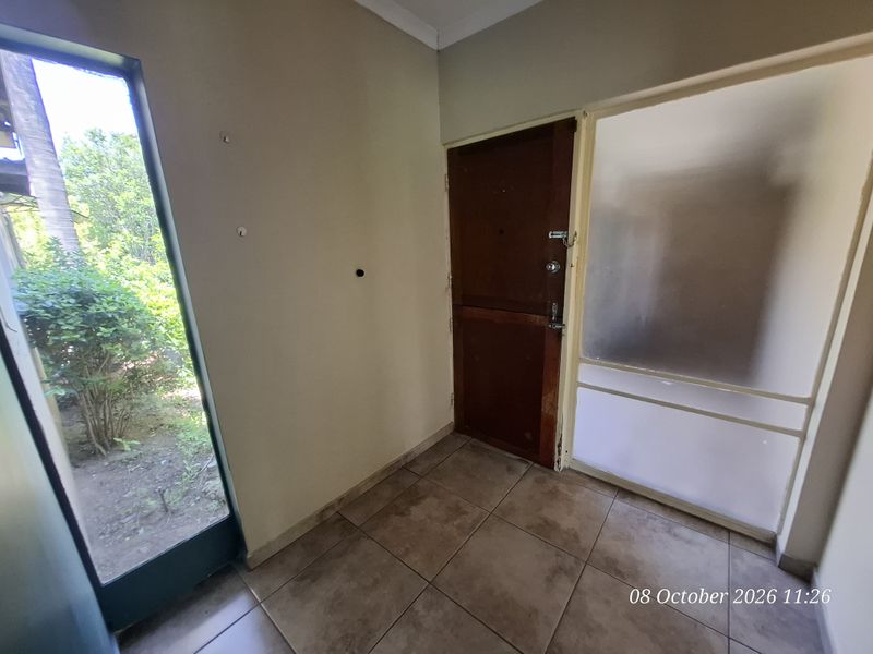 An empty entrance foyer featuring tiled flooring, a solid timber door, and a frosted glass sidelight providing natural light.