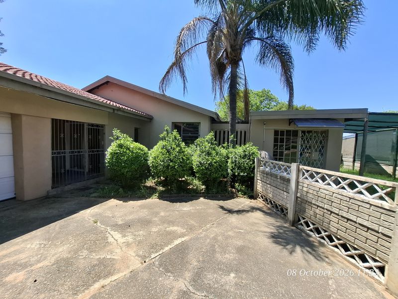 Front exterior view of the house featuring a concrete driveway, security gates, and a brick boundary wall under a clear blue sky.