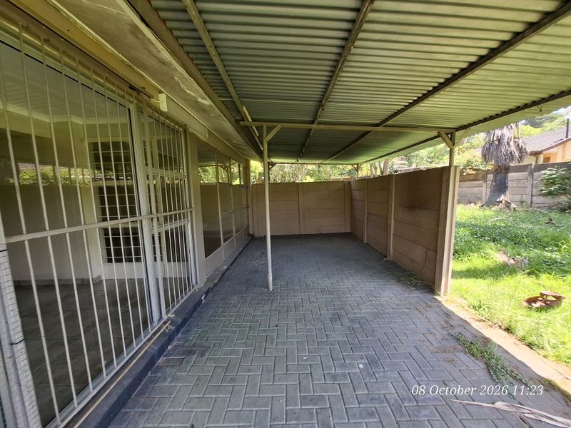 A covered outdoor patio area featuring paved flooring, a corrugated metal roof, and secure sliding glass door access to the main house interior.